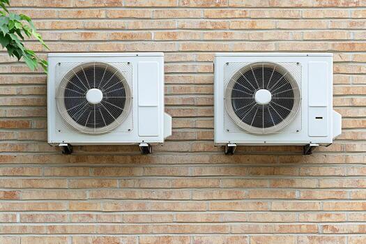 Two outdoor air conditioning units mounted side by side on a brick wall